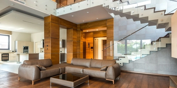 Das Bild zeigt ein modernes Wohnzimmer mit Holzverkleidungen an den Wänden, einem eleganten Holzboden und einer Decke mit eingebauten Spotlights. Eine stilvolle Treppe mit Glasgeländer ergänzt das Design. Große Fenster sorgen für viel Tageslicht.