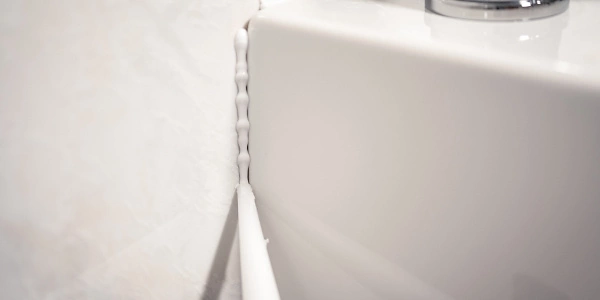 Eine Nahaufnahme einer weißen Badezimmerwand und einer Badewanne, verbunden durch eine frische Silikonfuge. Die Fuge sorgt für eine wasserdichte Abdichtung und ein sauberes Finish. Ideal für die Wartung und Pflege von Badezimmern.